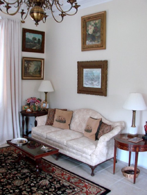 Cozy living room with a floral sofa, decorative pillows, a coffee table, lamps, and framed artwork on the walls.