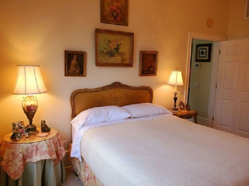 Cozy bedroom with a bed, two lamps, floral decor, and framed artwork on the walls.
