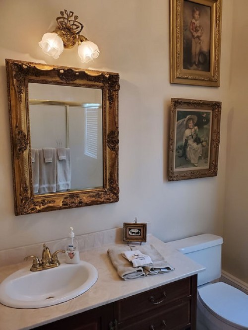 A vintage bathroom with ornate decor, featuring a mirror, sink, and framed artwork on the walls.