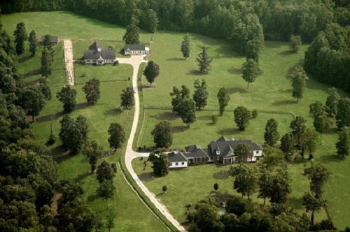 Aerial view of a spacious property with multiple houses, surrounded by trees and a winding driveway.