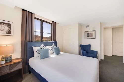 Cozy bedroom featuring a queen bed, decorative pillows, a chair, and large windows with natural light.