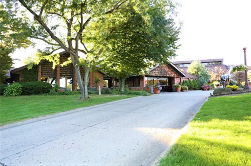 A scenic view of a building surrounded by trees and landscaped gardens, with a paved driveway leading up to it.