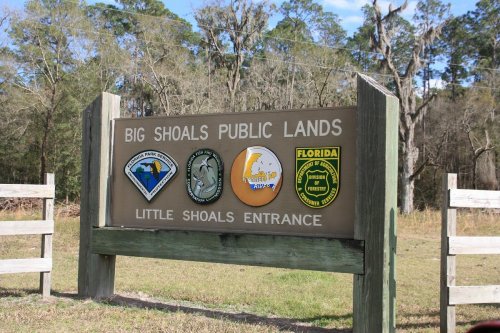 Sign for Big Shoals Public Lands at Little Shoals Entrance, featuring three logos and surrounded by trees.