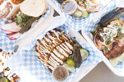 A variety of delicious Mexican dishes on blue checkered paper, featuring tacos, grilled chicken, and sauces with lime.