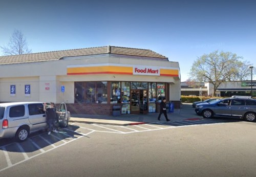 A Food Mart convenience store with a parking lot, featuring a few cars and a person getting out of a vehicle.