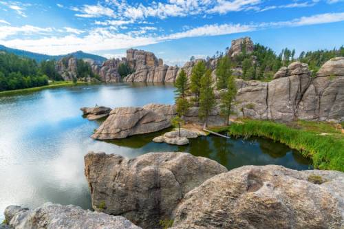 Scenic view of a calm lake surrounded by rocky formations and lush greenery under a blue sky with scattered clouds.