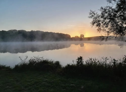 A serene lake at sunrise, with mist rising from the water and trees silhouetted against the colorful sky.