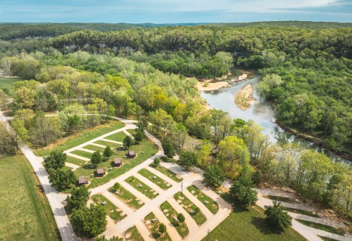 Aerial view of a green landscape with a river, campsites, and trees in a serene natural setting.