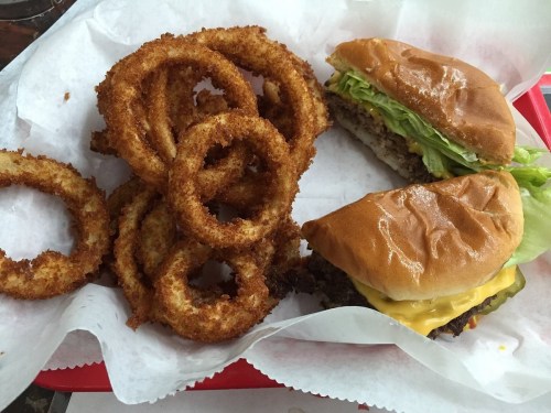 A plate with crispy onion rings and two cheeseburgers with lettuce on a red tray.