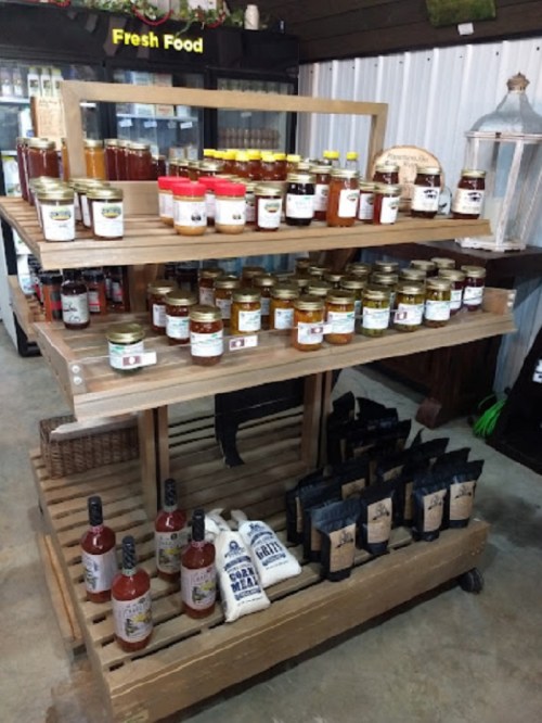 A wooden display shelf filled with jars of honey, sauces, and bags of spices in a rustic store setting.