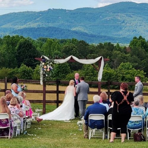 A wedding ceremony outdoors with guests seated, a couple at the altar, and mountains in the background.