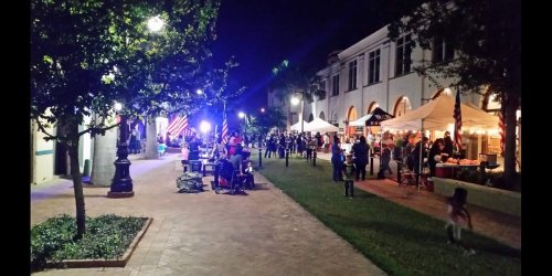 A lively night scene with people gathered at an outdoor event, featuring tents, lights, and festive decorations.