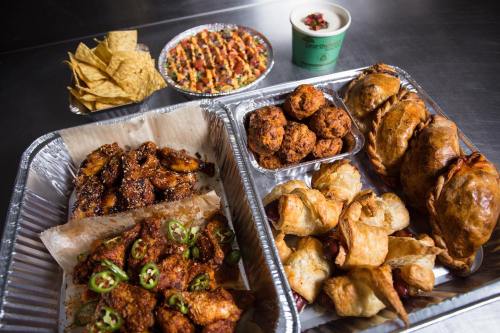 A variety of delicious foods including wings, pastries, nachos, and a colorful dish in a bowl, all served in trays.