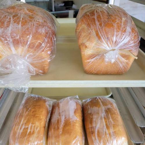 Two loaves of bread wrapped in plastic on a shelf, with additional loaves visible below.