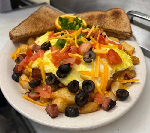A hearty breakfast plate with an omelet, diced tomatoes, olives, cheese, hash browns, and toast, garnished with parsley.