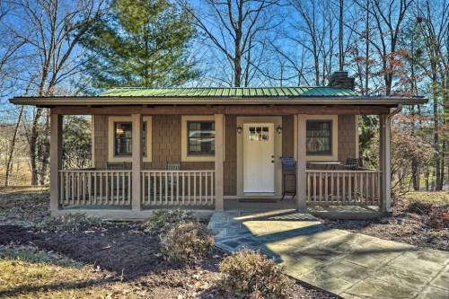 A cozy cabin with a green metal roof, front porch, and surrounded by trees on a sunny day.