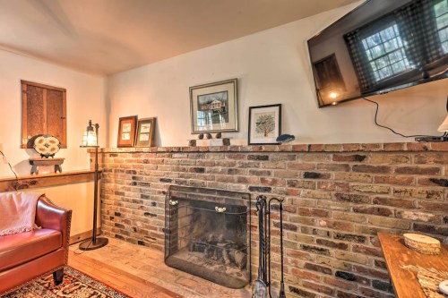 Cozy living room with a brick fireplace, framed art, a TV, and a leather chair, creating a warm atmosphere.