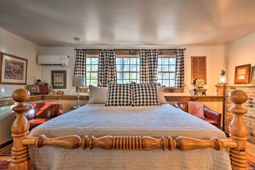 Cozy bedroom with a large bed, checkered curtains, and warm wooden accents, featuring two armchairs and decorative artwork.