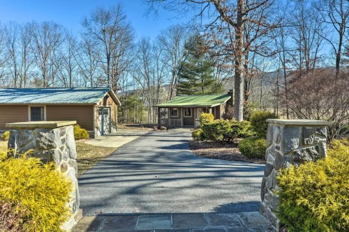 A scenic driveway leads to a cozy cabin surrounded by trees and greenery under a clear blue sky.