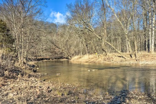 A serene river flows through a wooded area, with bare trees and a clear blue sky above.