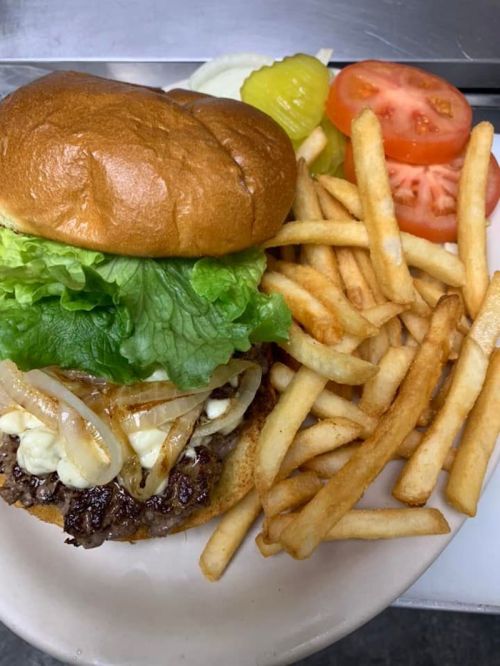 A juicy burger with lettuce, onions, and mayo, served with fries and fresh tomato and pickle slices on the side.