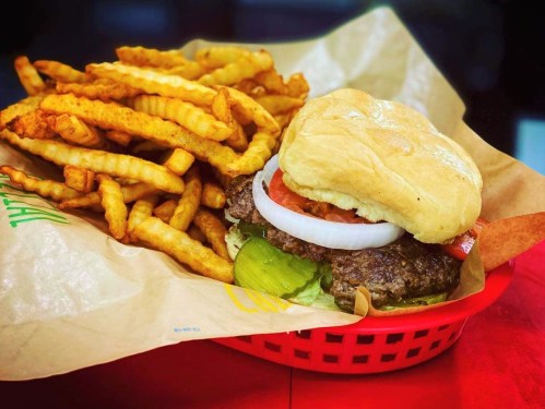 A juicy burger with lettuce, tomato, onion, and pickles, served with a side of crispy crinkle-cut fries in a basket.