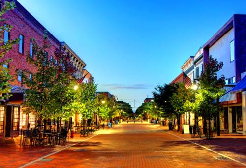 A quiet, tree-lined street at dusk, featuring brick buildings and outdoor seating under soft streetlights.
