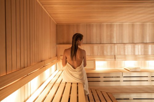 A person sitting on a wooden bench in a sauna, wrapped in a towel, with warm lighting and wooden walls.