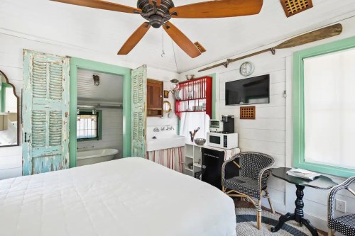 Cozy room with a bed, vintage decor, kitchenette, and a ceiling fan, featuring light wood and turquoise accents.
