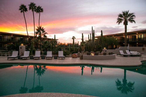 A serene poolside scene at sunset, with palm trees and cacti reflecting in the water.