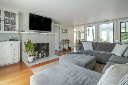 Cozy living room with a gray sectional sofa, a TV above a fireplace, and large windows letting in natural light.