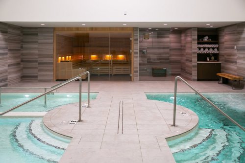A modern spa area featuring two hot tubs, wooden accents, and a sauna in the background. Relaxing atmosphere.