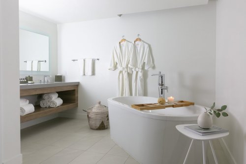 A modern bathroom featuring a freestanding tub, wooden vanity, white robes, and soft towels, creating a serene atmosphere.