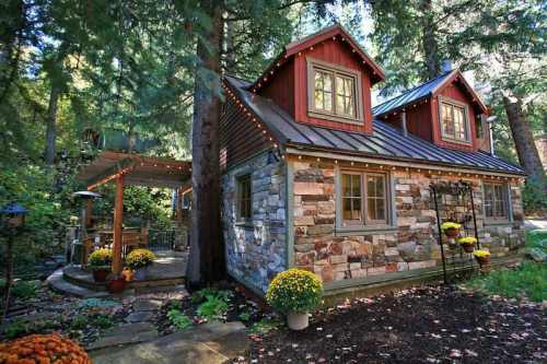 Charming stone cottage surrounded by trees, featuring a cozy patio and colorful flowers.