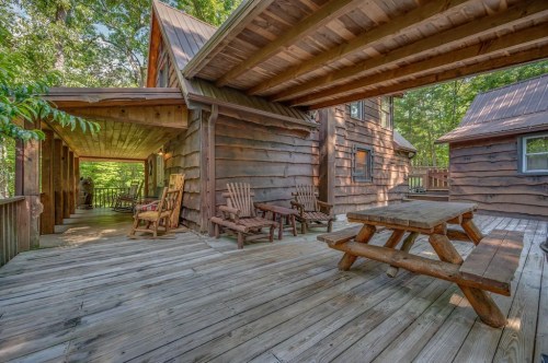 A rustic wooden cabin with a spacious porch, rocking chairs, and a picnic table surrounded by trees.