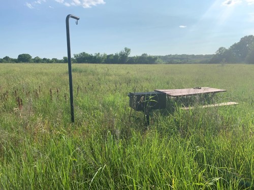 A picnic table and a water spigot stand in a grassy field under a clear blue sky.