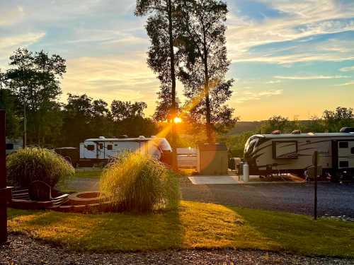 Sunset over a campground with RVs, surrounded by lush greenery and a fire pit in the foreground.