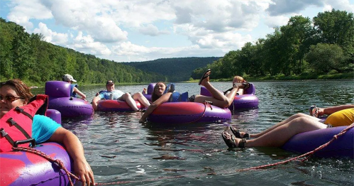 A group of people relaxing on colorful inner tubes in a river, surrounded by lush greenery and a blue sky.