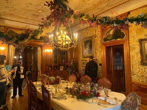 A beautifully decorated dining room with a festive table setting, ornate wallpaper, and guests admiring the decor.