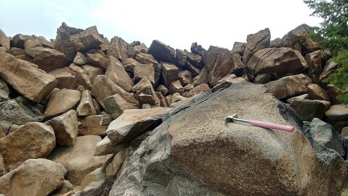 A close-up of a large rock with a pink hammer resting on it, surrounded by a pile of boulders in the background.