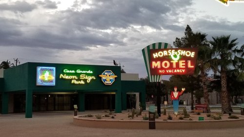 A colorful neon sign for the Horseshoe Motel with a "No Vacancy" message, set against a cloudy sky.