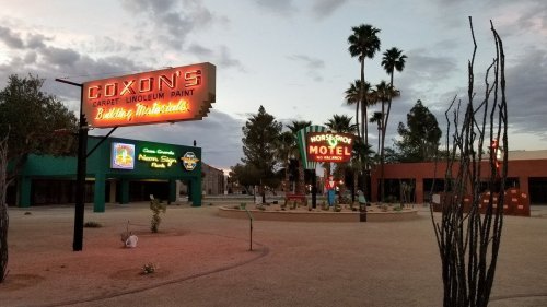 Vintage neon signs for Coxon's and Horseshoe Motel in a deserted area with palm trees and a cloudy sky.
