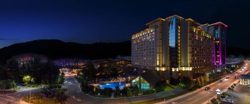A panoramic view of a brightly lit hotel complex at night, featuring a pool and surrounding mountains.