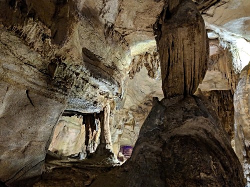 A dimly lit cave interior featuring textured rock formations and stalactites hanging from the ceiling.