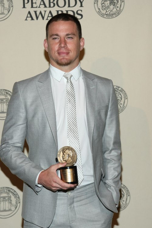 Channing Tatum in a light gray suit holding a Peabody Award at an awards ceremony backdrop.