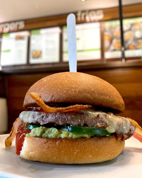 A close-up of a burger with bacon, cheese, and guacamole on a toasted bun, served on a plate.