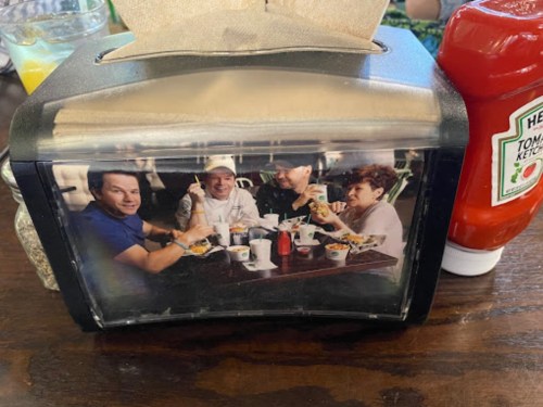 A condiment holder on a table featuring a photo of four people enjoying food together. Ketchup and salt are nearby.