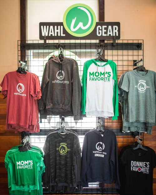 A display of Wahlburgers merchandise, including hoodies and shirts, hanging on a grid wall.