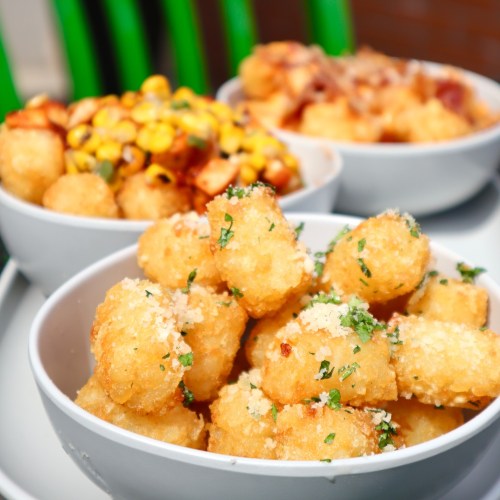 Three bowls of crispy snacks: one with cheesy tater tots, one with corn salad, and another with loaded tater tots.