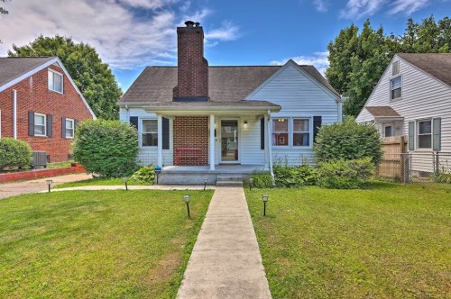 A charming blue house with a chimney, surrounded by greenery and a clear sky, featuring a walkway leading to the front door.
